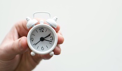 A hand holds a white alarm clock.