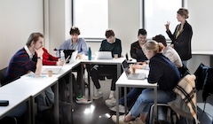 A group of 8 students sit in a classroom with their computers open.